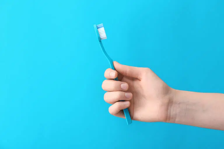 Hand with toothbrush on color background