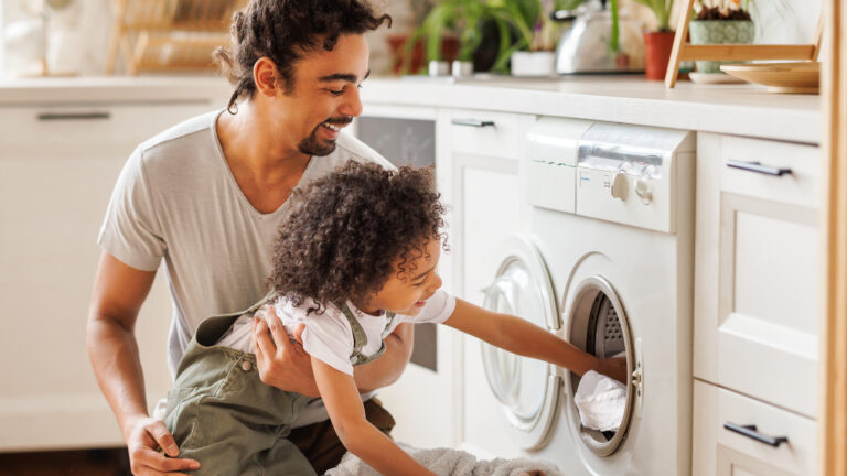 Son helping dad to load washing machine, man child doing laundry
