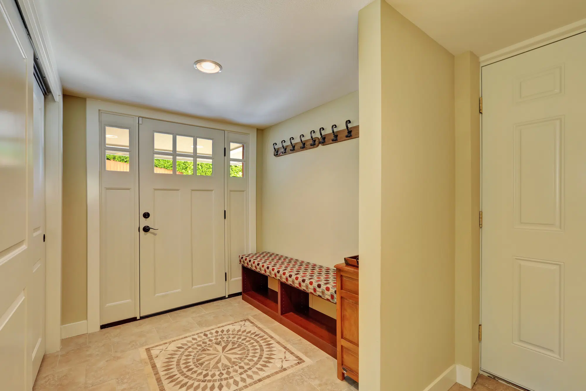 Entryway in light tones with mosaic tile floor, bench seat, built-in wardrobe and hangers on the wall. Northwest, USA