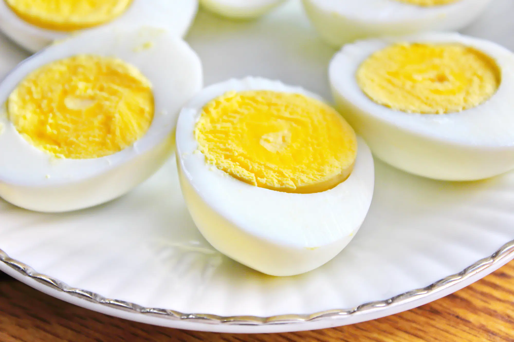 Half boiled eggs laid out in white plates and served on a wooden table.