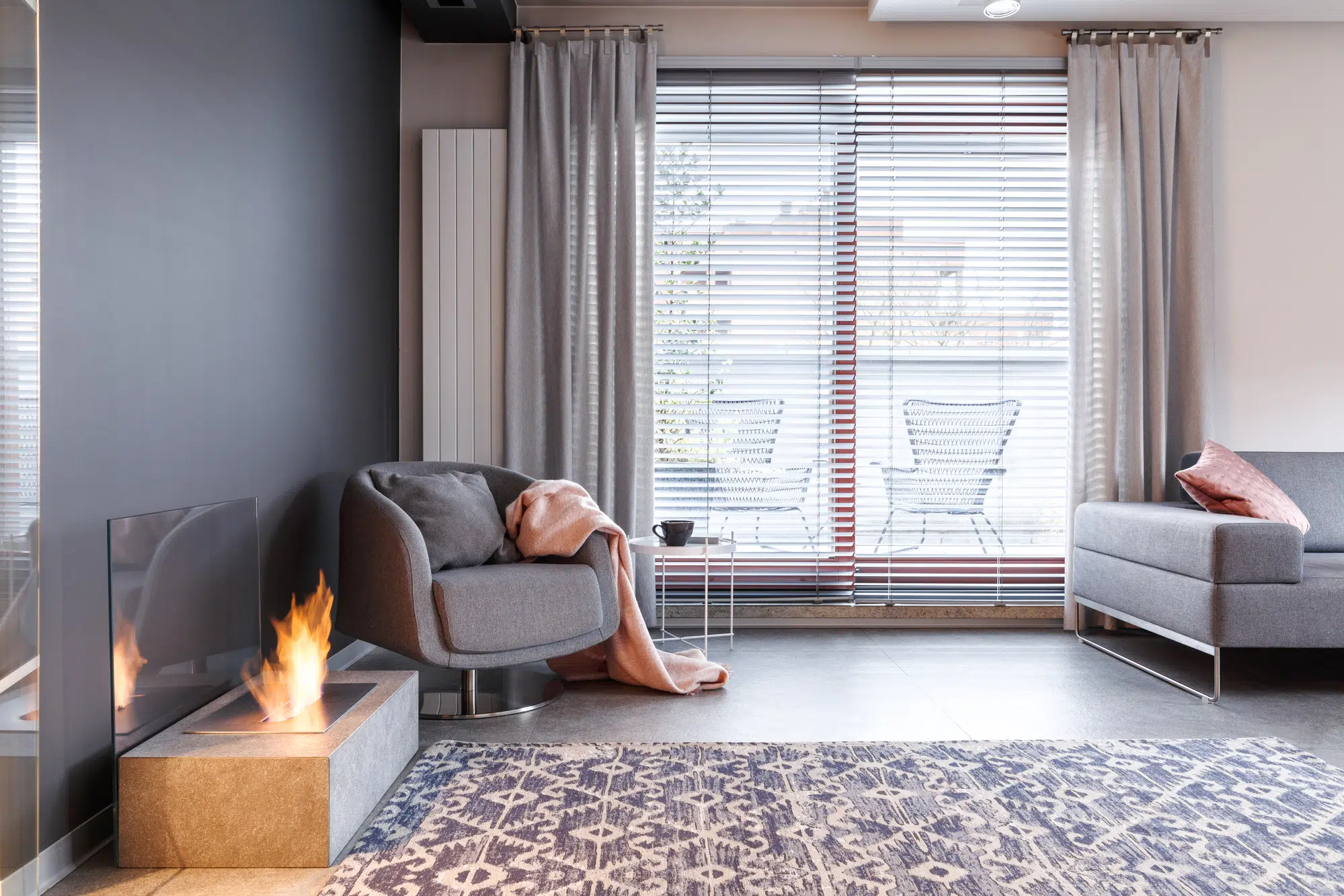 Patterned carpet and grey armchair with pink blanket near fireplace in contemporary apartment interior