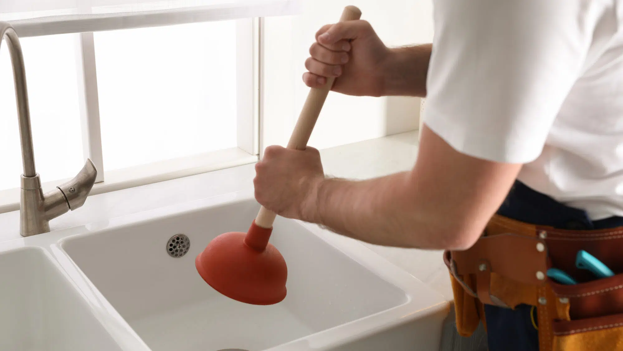 Plumber using plunger to unclog sink drain in kitchen, closeup